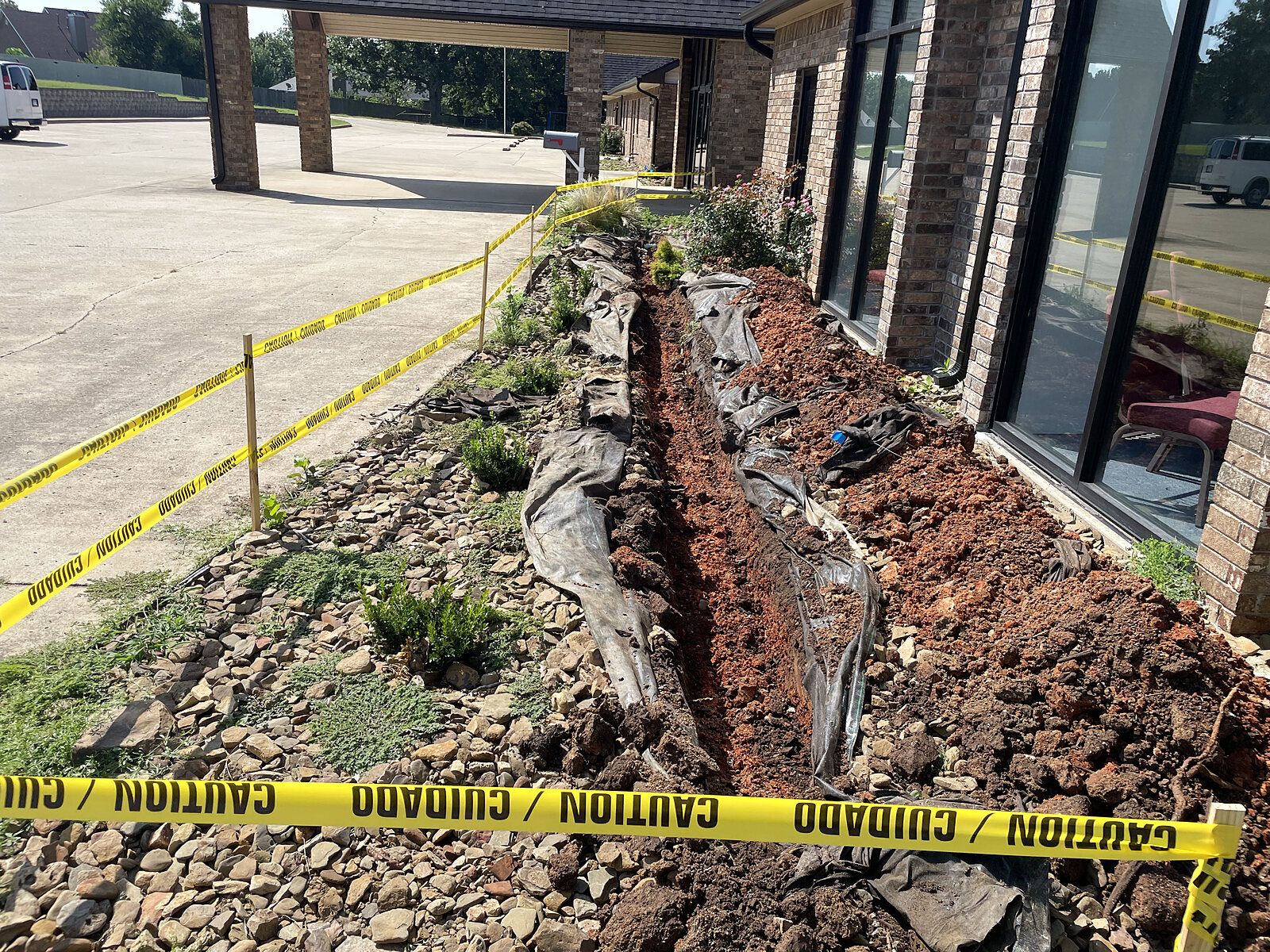 Trench dug through a landscape bed with drainage fabric laid in