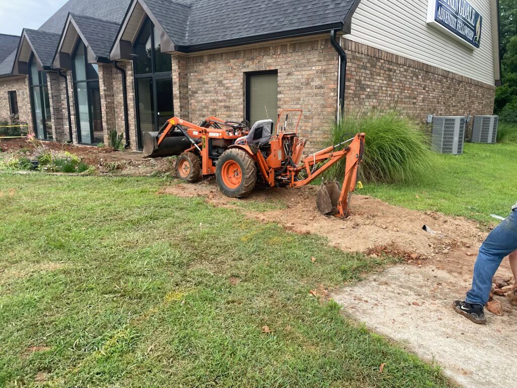 Compact tractor backhoe digging beside a commercial building without damaging the lawn