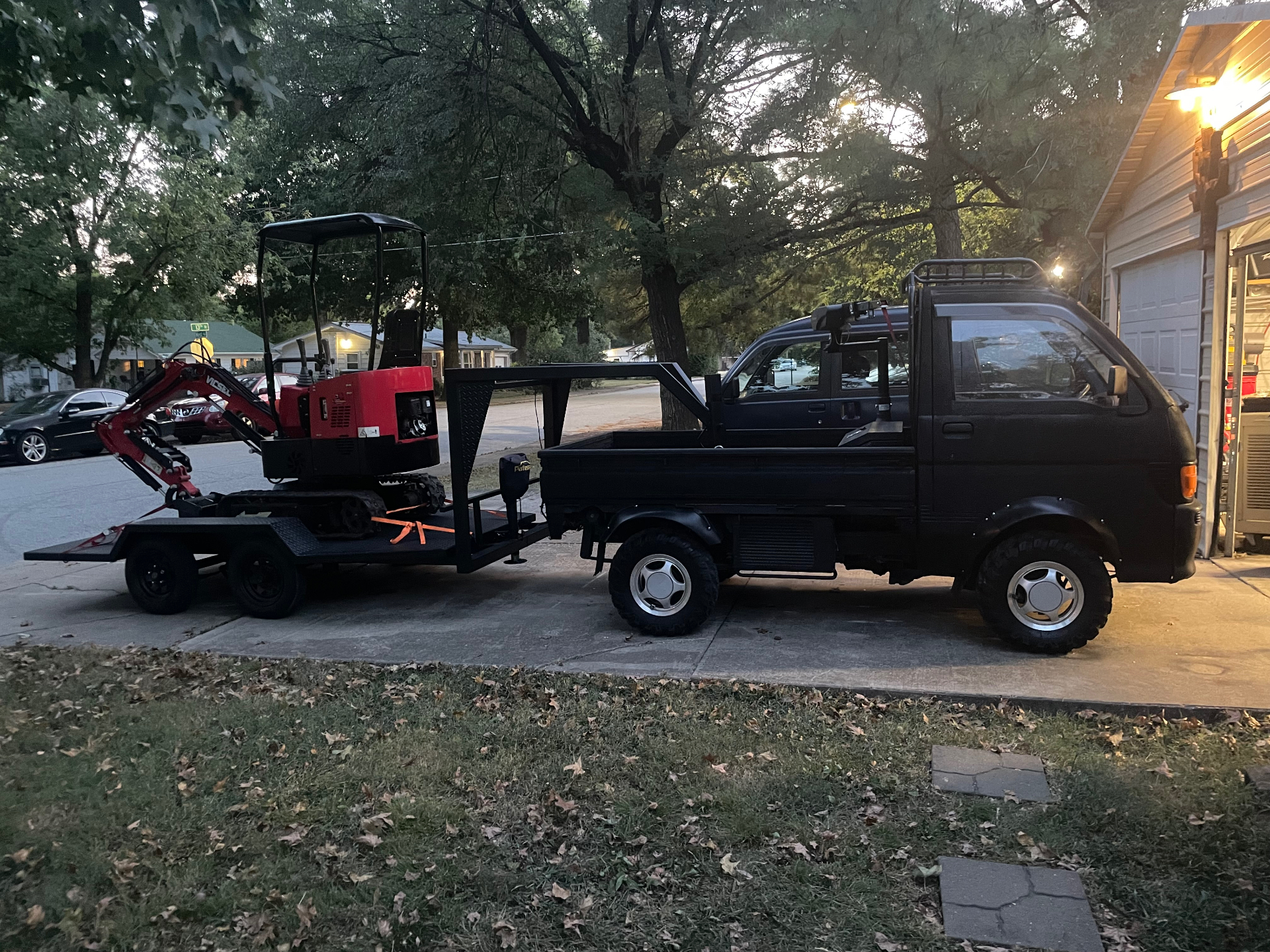 Black mini truck hauling a red excavator on a custom trailer